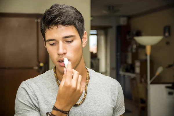 Beau jeune homme appliquant baume à lèvres à la maison — Photo