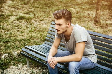 Parktaki bankta oturan yakışıklı sarışın genç adam.