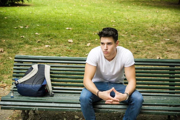 Joven estudiante masculino sentado en Banco de parque en serio —  Fotos de Stock