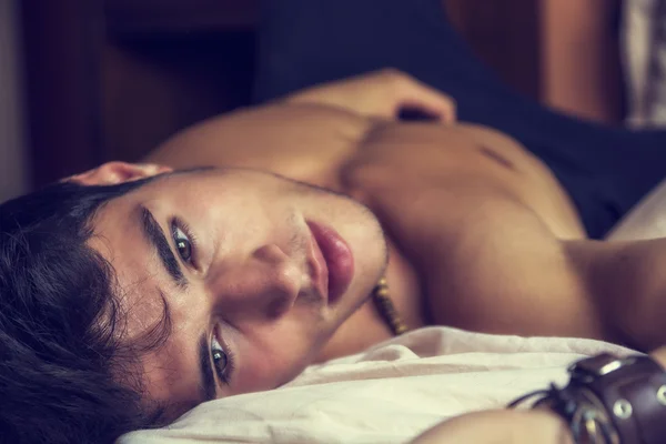 Tişörtsüz seksi erkek model yatağında tek başına yatıyor.