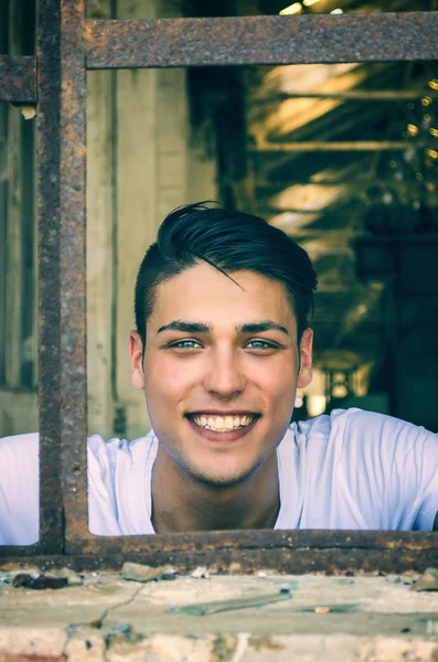 Handsome young man with happy expression in rusty window — Stock fotografie