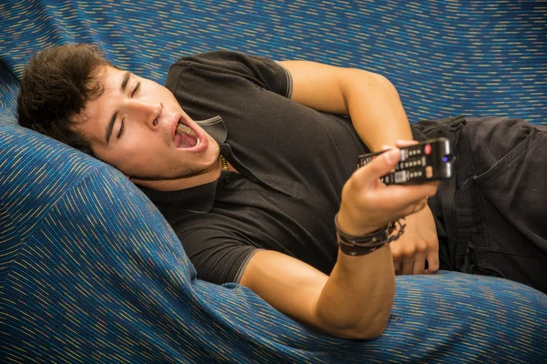 Young bored man sitting on sofa watching television — Stock Photo, Image