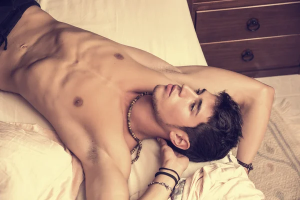 Shirtless sexy male model lying alone on his bed — Stock Photo, Image