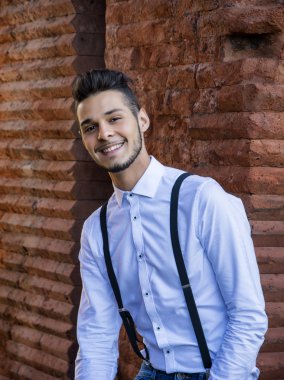 Çekici bir genç adam tuğla duvarda oturuyor.