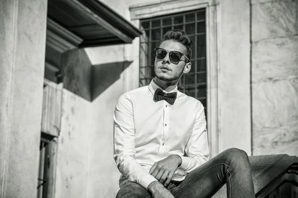 Atractivo hombre joven sentado en la ciudad de usar gafas de sol —  Fotos de Stock