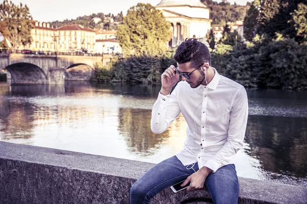 Hombre joven contemplativa sentado al lado del río — Foto de Stock