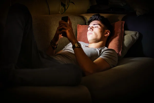 Jeune homme sur le canapé, éclairé par la lumière du téléphone cellulaire — Photo