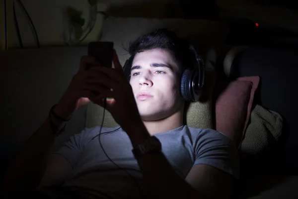 Jeune homme sur le canapé, éclairé par la lumière du téléphone cellulaire — Photo