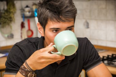 Young Man Drinking Coffee Sitting at Kitchen Table