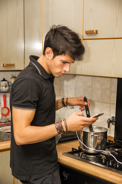 Young Man with Cell Phone Cooking Food on Stove — Zdjęcie stockowe