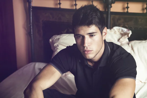 Handsome young man sitting on his bed — Stock Photo, Image