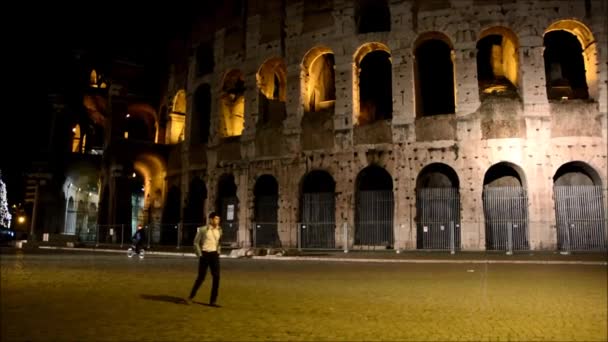 Ung man går framför Colosseum i Rom, Italien, på natten — Stockvideo