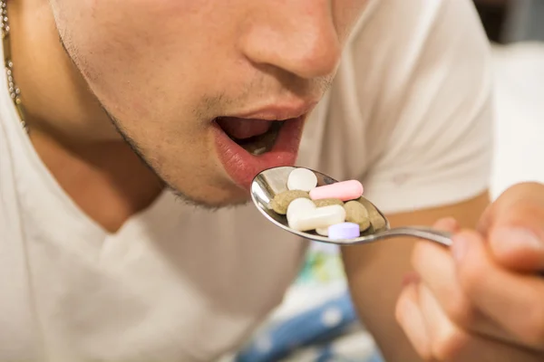 若い男は薬でいっぱいのスプーンを食べる — ストック写真