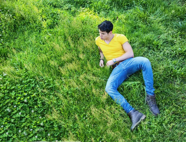 Jovem bonito apto relaxantes deitado no gramado — Fotografia de Stock