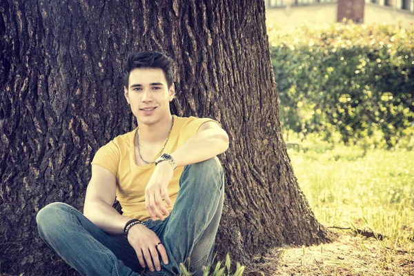 Attraente giovane uomo nel parco che riposa contro l'albero — Foto Stock