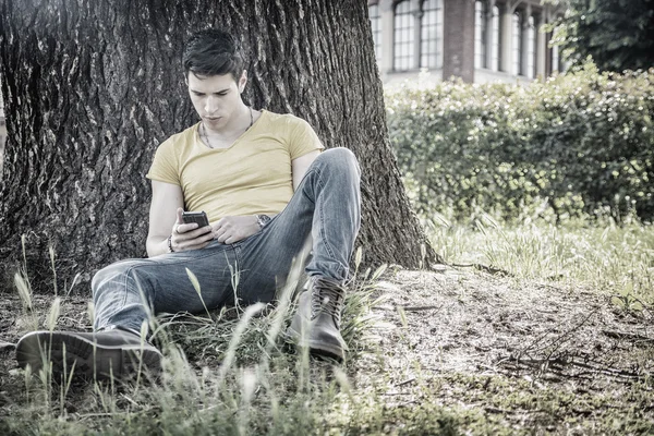 Jeune homme attrayant dans le parc reposant contre l'arbre — Photo