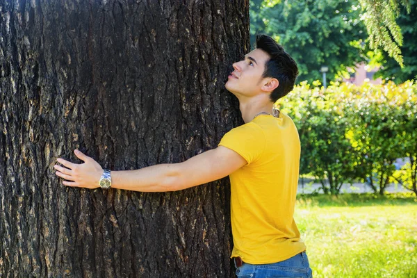 Smiling young man hugging a tree, looking up — Stock Photo, Image