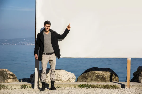 Young man standing next to large blank white billboard, display — Stock Photo, Image