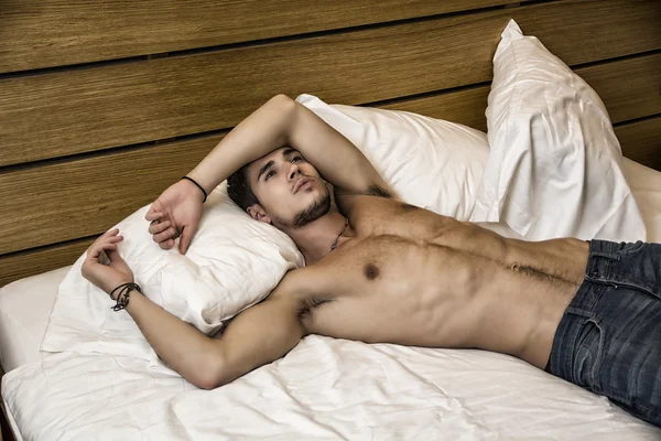 Shirtless sexy male model lying alone on his bed Stock Image