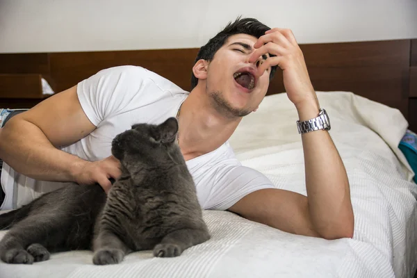 Mann, liegend auf dem Bett schmusen Katze und Niesen — Stockfoto