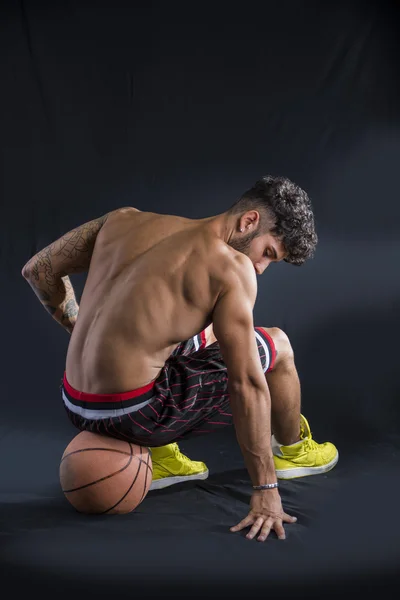 Jonge atletische man zit op basketbal bal — Stockfoto