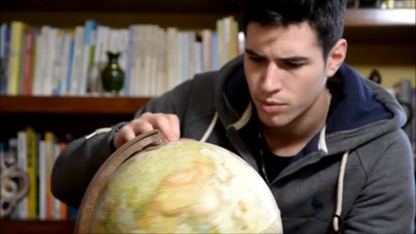 Beau jeune homme tenant un globe à l'intérieur à la maison en regardant la caméra — Video