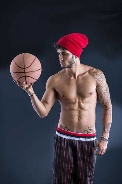 Młody człowiek lekkoatletycznego na ciemnym tle trzymając piłkę do koszykówki — Zdjęcie stockowe