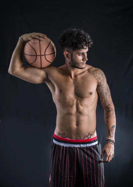 Jovem Atlético no fundo escuro, segurando uma bola de basquete — Fotografia de Stock