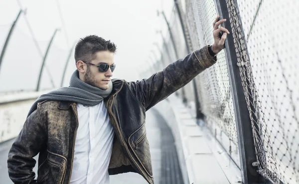 Handsome trendy man standing on a bridge, looking down — Stok Foto