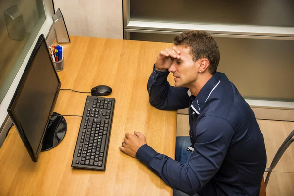 Worried young businessman sitting at desk — Stock fotografie