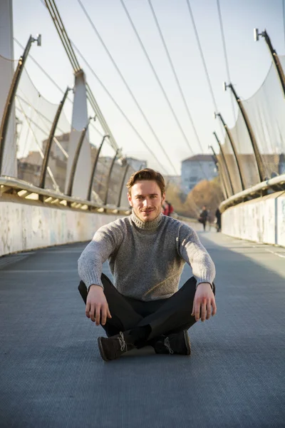 Knappe jonge man zitten buiten in stedelijke omgeving — Stockfoto