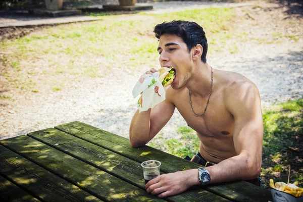 Young Man Having Fast Food Lunch at Picnic Table — Stock Photo, Image