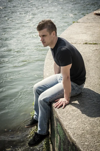 Contemplative teenage boy sitting beside river — Stock Photo, Image