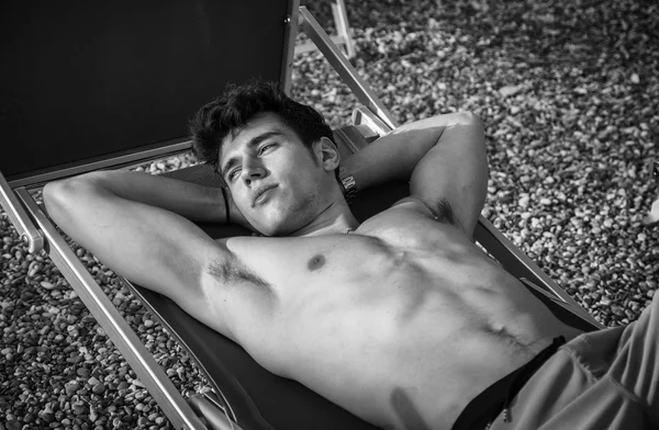 Plajda şezlong güneşlenme gömleksiz genç adam — Stok fotoğraf
