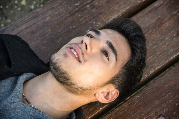 Close-up of young man lying on bench and looking up — kuvapankkivalokuva