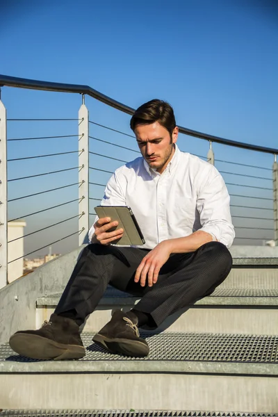 Hombre de moda guapo mirando hacia abajo en una tableta, al aire libre —  Fotos de Stock