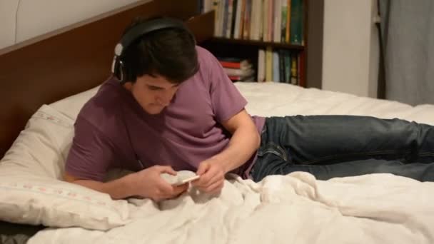 Knappe jonge man in bed luisteren naar muziek — Stockvideo