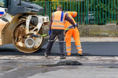 Paving işçileri tekerlek silindirinin önüne asfalt eklediler - yol yeniden yapılandırması