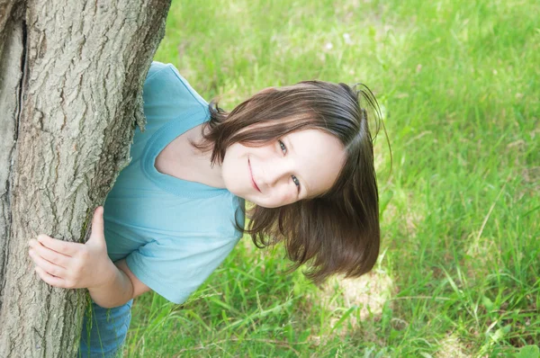 Chica mira hacia fuera desde detrás de un árbol —  Fotos de Stock