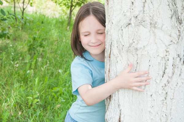 Chica mira hacia fuera desde detrás de un árbol — Foto de Stock