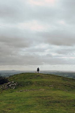Kimliği belirsiz bir adam ve bir köpeğin Mendip Hills, İngiltere 'de bir tepenin tepesinde gökyüzüne karşı yürüdüğü görüntüler..
