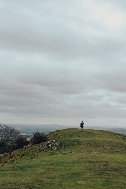 Kimliği belirsiz bir adam ve bir köpeğin Mendip Hills, İngiltere 'de bir tepenin tepesinde gökyüzüne karşı yürüdüğü görüntüler..