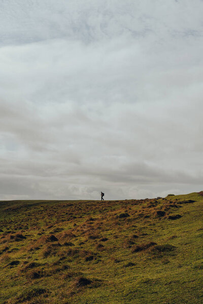 Unidentifiable man walking on the horizon line on top of a hill in Mendip Hills, UK, against the sky.
