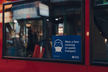 Londra, İngiltere - 5 Aralık 2020: Londra 'da kırmızı çift katlı bir otobüsün camına bir maske takın. Bu gereksinimler Coronavirus salgını nedeniyle getirildi..