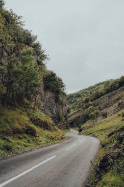 Cheddar Gorge, UK - July 26, 2020: Road going through Cheddar Gorge, a famous limestone gorge in the Mendip Hills, near the village of Cheddar, Somerset, England. People walking in the distance.