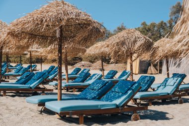 Yunanistan 'ın Mykonos kentinde güneşli bir yaz gününde şemsiyelerin altında boş mavi güneş yatakları ve şezlonglar.