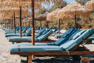 Yunanistan 'ın Mykonos kentindeki bir plajda şemsiyelerin altında boş mavi güneş yatakları ve şezlongların yan görüntüsü.