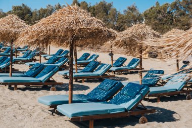 Yunanistan 'ın Mykonos kentinde güneşli bir yaz gününde şemsiyelerin altında boş mavi güneş yatakları ve şezlonglar.
