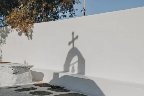Shadow from the cross and bell on top of a church falling on a whitewash wall in Ana Mera, Mykonos, Greece.
