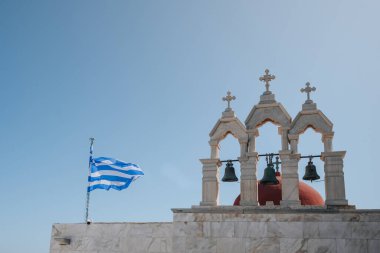 Ana Mera, Yunanistan - 24 Eylül 2019: Panagia Tourliani Manastırı 'nda Yunan bayrağı ve çanları, Mikonos' ta 16. yüzyıldan kalma beyaz boyalı bir kilise ve manastır, bulanık gökyüzüne karşı.